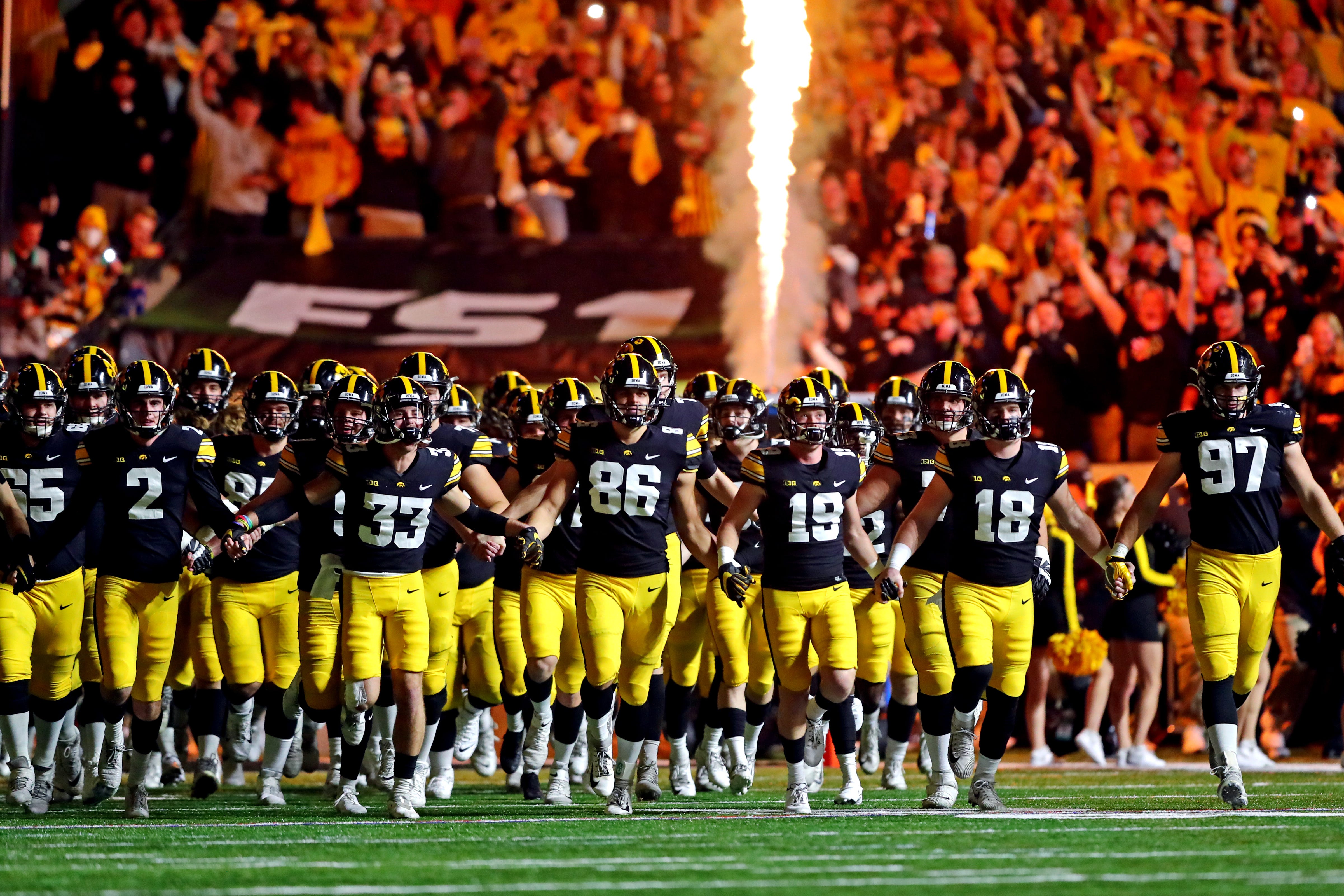 Iowa Hawkeyes players hold hands as the run onto the field before playing the Michigan Wolverines in the Big Ten Conference championship game, Saturday, Dec. 4, 2021, at Lucas Oil Stadium in Indianapolis, Ind.